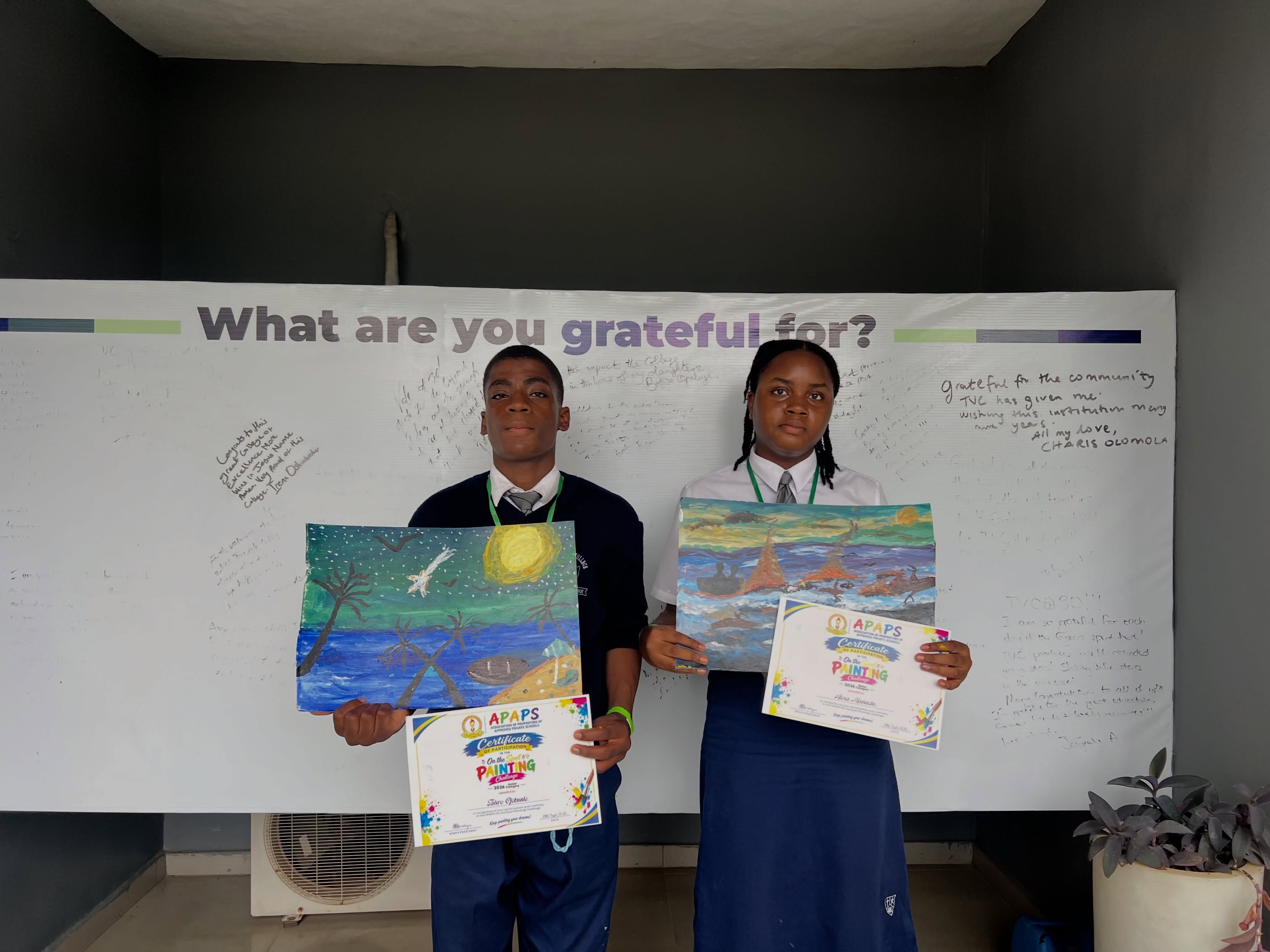 Two Vale College students displaying paintings and certificates